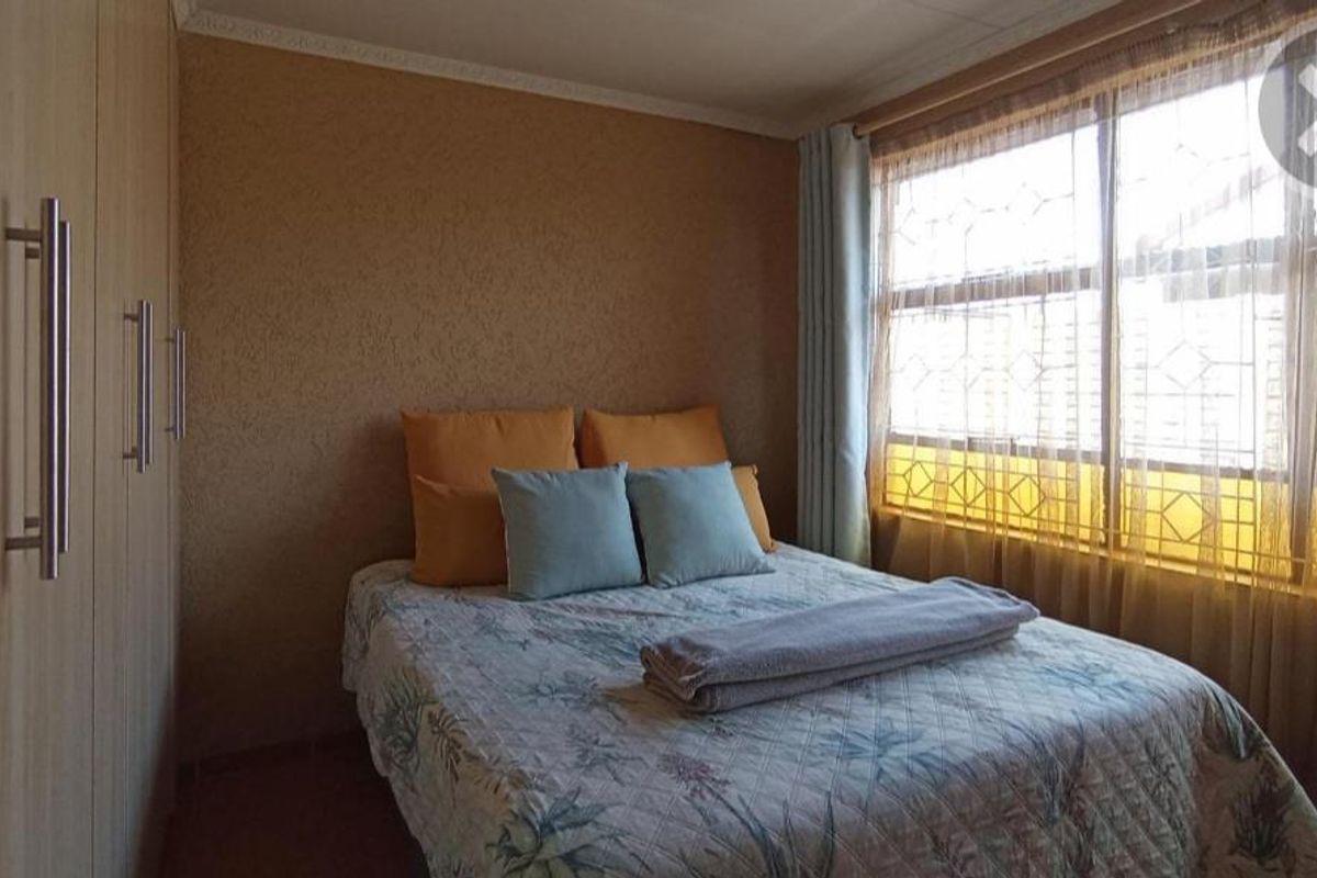 A cozy bedroom featuring built-in wooden wardrobes and large windows that allow for natural light.