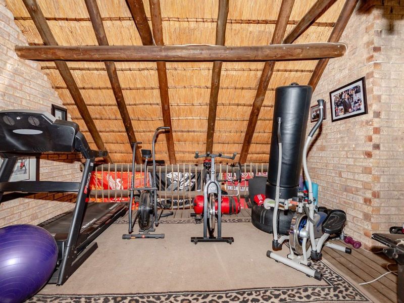 A rustic home gym located in an attic space featuring exposed timber rafters, a thatched roof, and exposed brick walls.