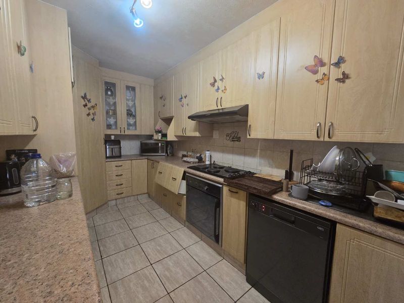 A functional kitchen featuring light wood-finish cabinetry, tiled flooring, and built-in appliances, offering a practical layout with ample storage space.