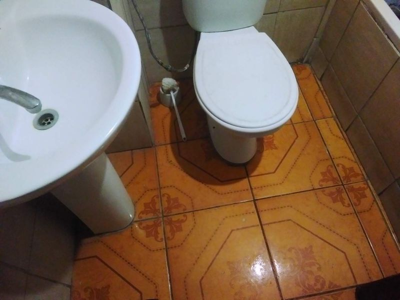 A compact bathroom featuring a pedestal sink and toilet with dated orange patterned ceramic floor tiles and wall tiling.