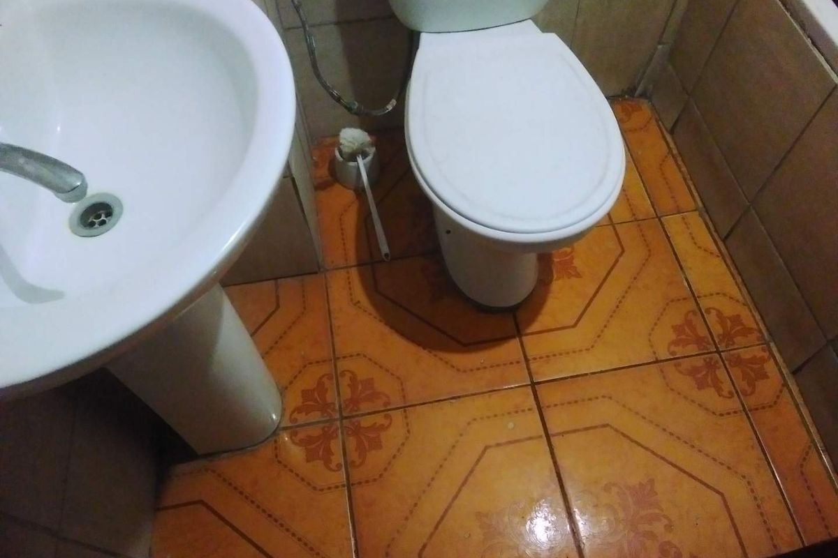 A compact bathroom featuring a pedestal sink and toilet with dated orange patterned ceramic floor tiles and wall tiling.