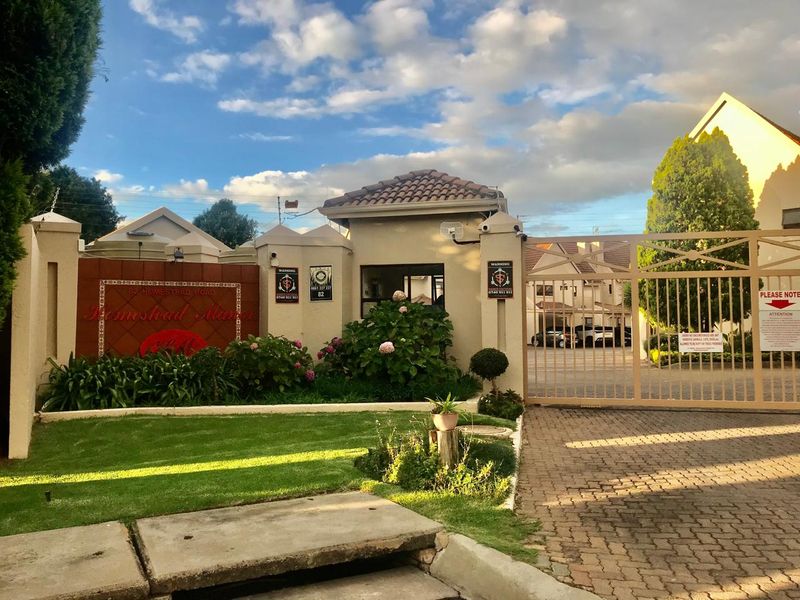The secure entrance to Homestead Manor townhouse complex, featuring a gated driveway, perimeter wall, and well-maintained landscaped garden.