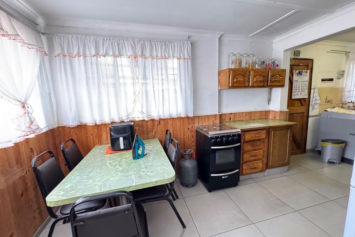 A dated kitchen area featuring timber wall paneling, tiled flooring, and a freestanding stove, with an adjacent scullery or utility space visible.