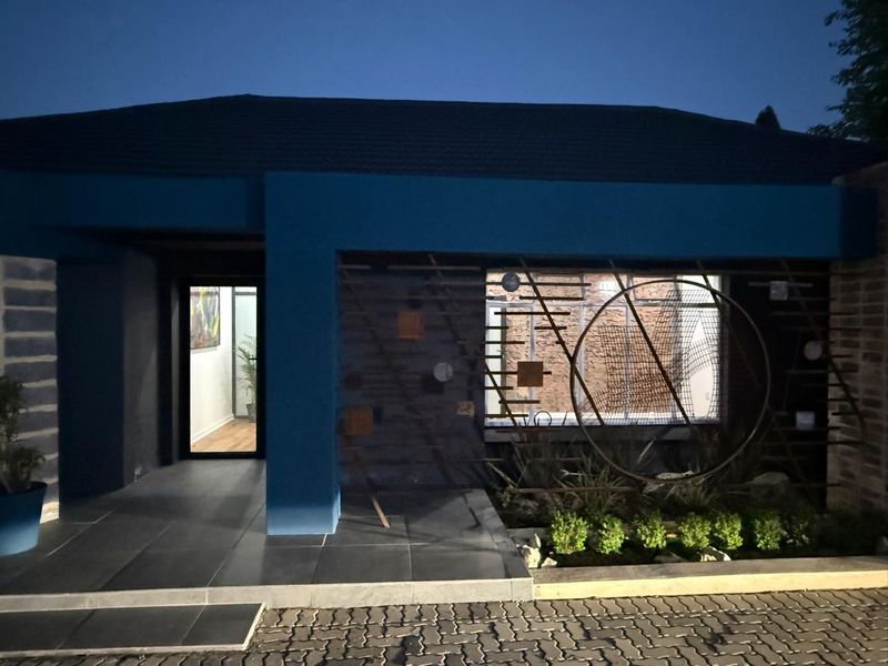 Modern business entrance featuring a tiled porch, decorative metal facade screen, and landscaped garden bed, illuminated at dusk.