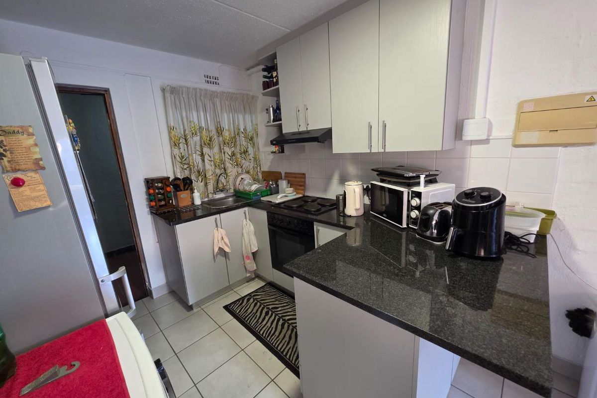 Compact kitchen featuring granite countertops, built-in cabinetry, an integrated stove and oven, and tiled flooring.