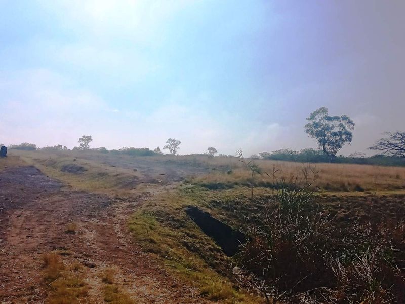 A view of the vacant commercial land featuring perimeter security fencing with razor wire and natural drainage terrain.