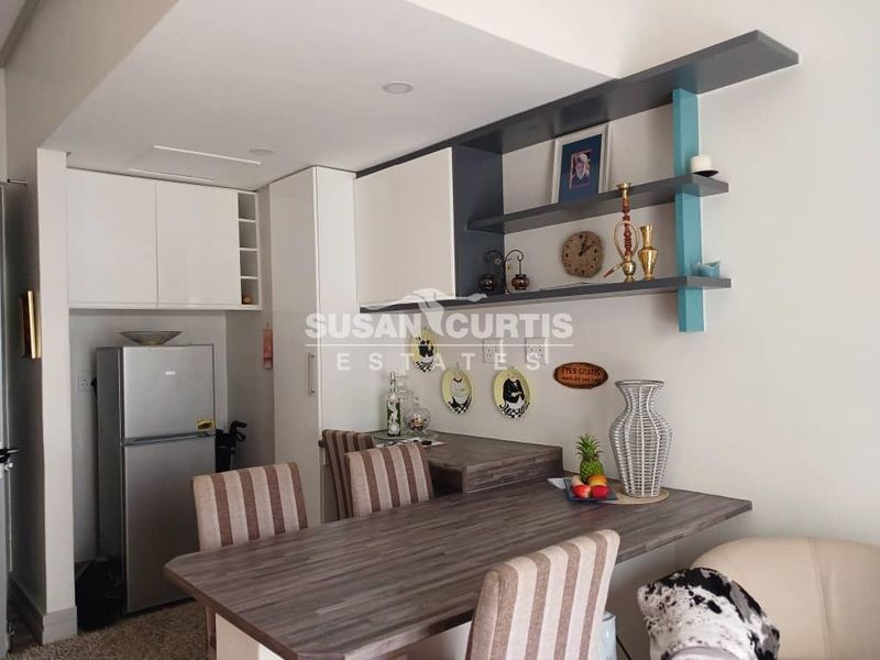Compact kitchen area featuring modern white cabinetry, open shelving, and a functional laminate breakfast bar for casual dining.