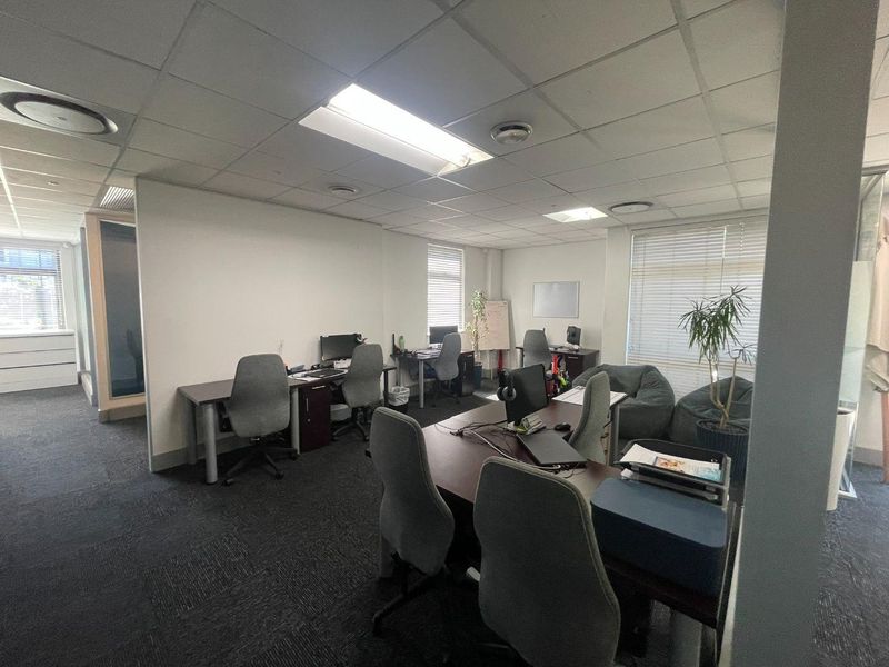 A functional open-plan office space featuring suspended ceilings, recessed lighting, and carpeted flooring with multiple workstation areas.