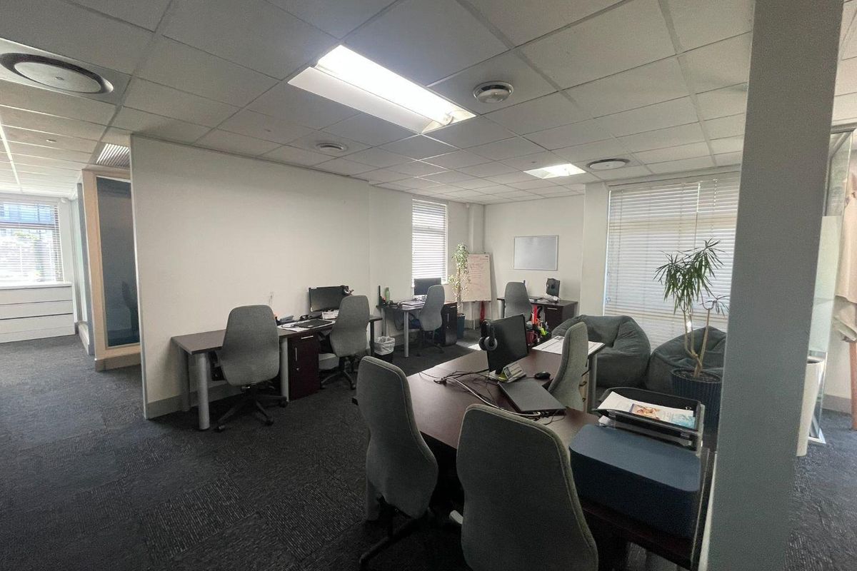 A functional open-plan office space featuring suspended ceilings, recessed lighting, and carpeted flooring with multiple workstation areas.