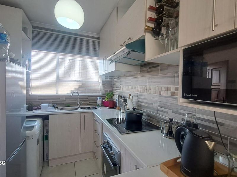 A compact, functional kitchen featuring light-toned cabinetry, a tiled backsplash, integrated appliances including an oven and hob, and a stainless steel sink.