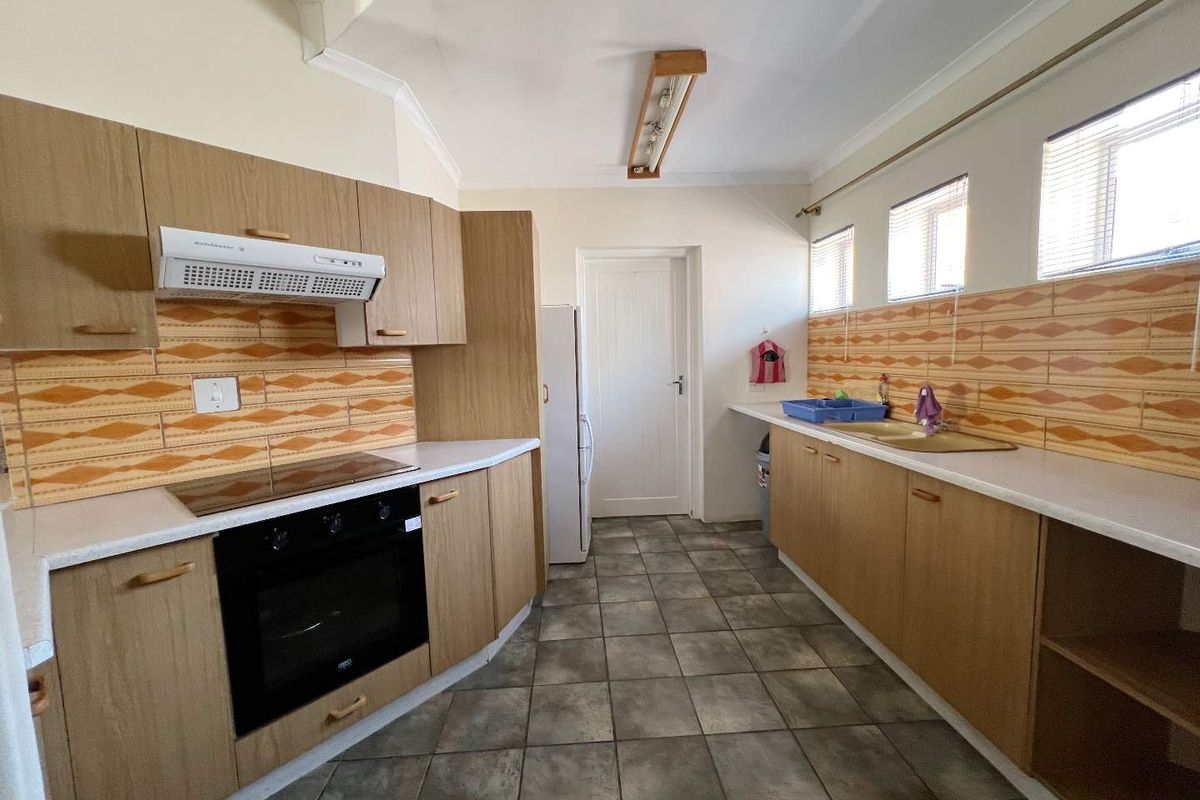 A functional kitchen featuring wood-look cabinetry, built-in oven and hob, extractor fan, and tiled flooring with a classic backsplash.