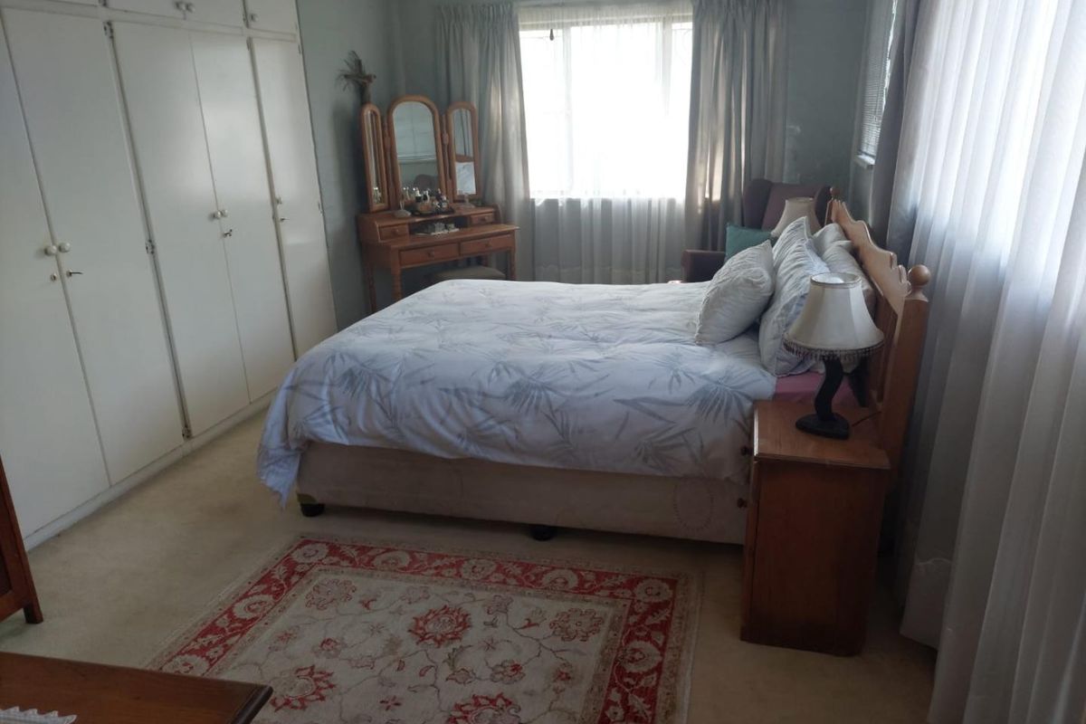 A well-proportioned bedroom featuring built-in cupboards and carpeted flooring, offering a functional space with natural light.