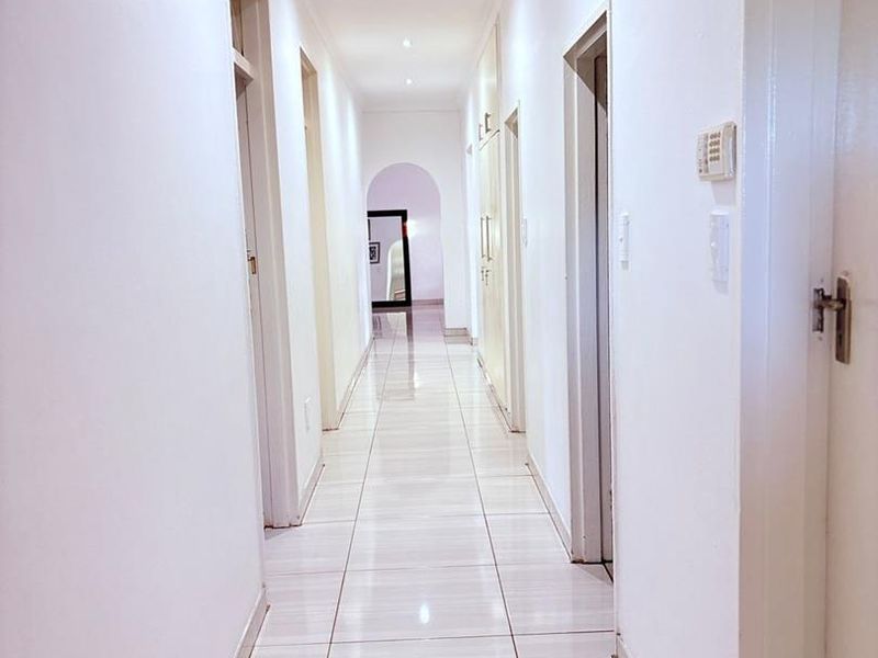 A bright, well-maintained hallway featuring neutral tiled flooring, recessed downlighting, and built-in storage cupboards leading to an arched transition.