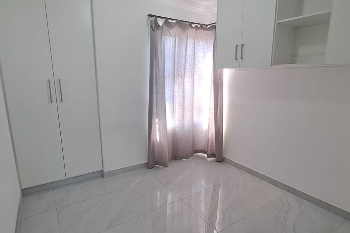 A bright, empty bedroom featuring modern tiled flooring, ample built-in cupboard space, and additional overhead storage cabinets.