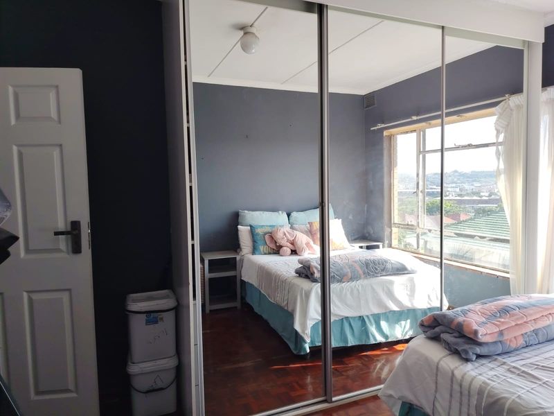 Bedroom featuring parquet flooring, a large window with natural light, and a full-length built-in mirrored wardrobe.