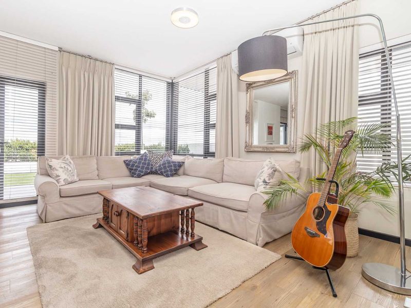 A bright and airy living room featuring laminate flooring, large windows with blinds, and a wall-mounted air conditioning unit.