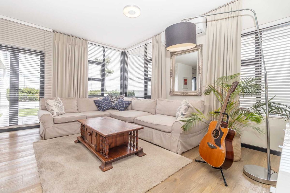A bright and airy living room featuring laminate flooring, large windows with blinds, and a wall-mounted air conditioning unit.