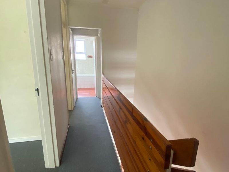 A functional hallway featuring a timber balustrade and staircase, leading towards a bathroom area with tiled flooring.