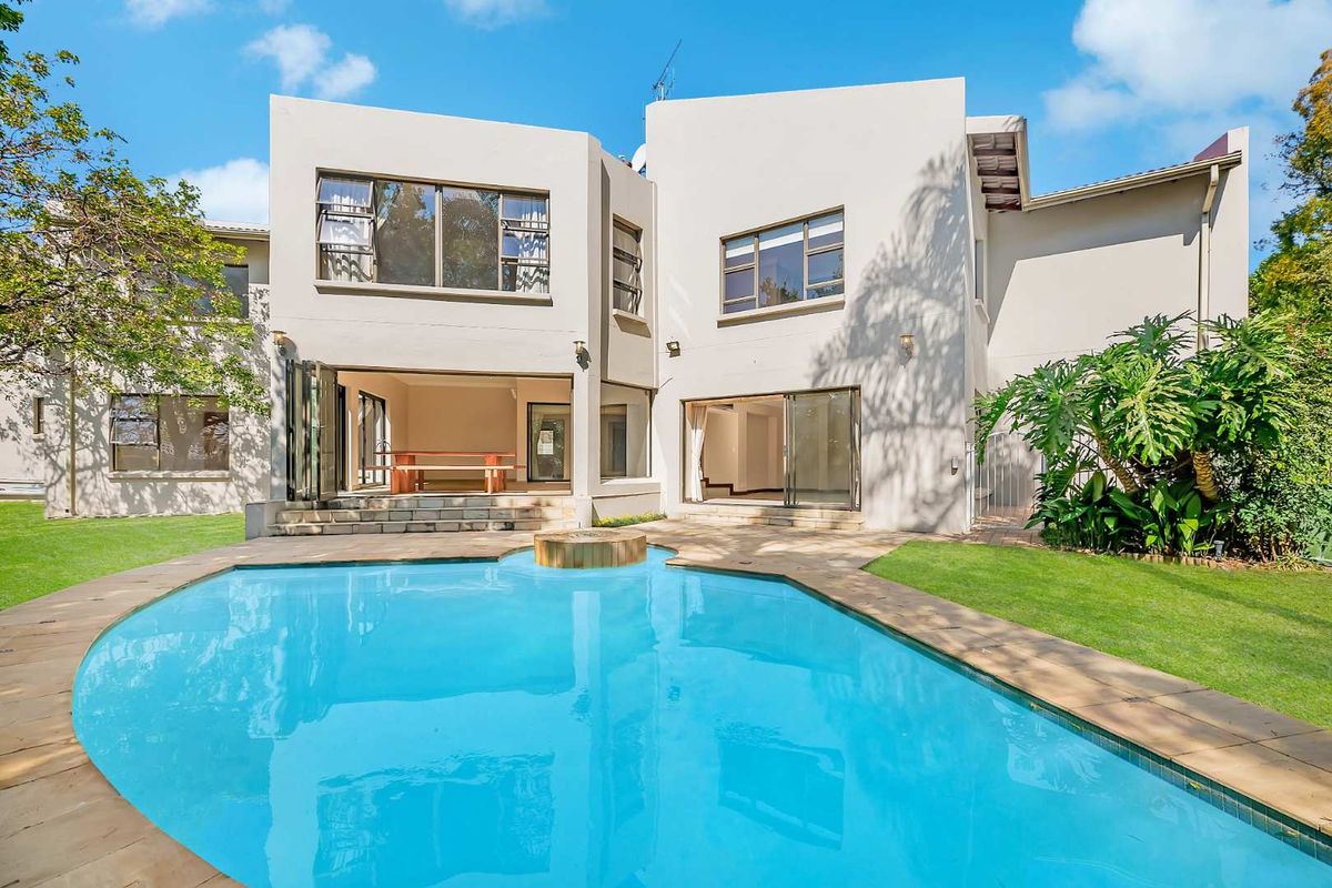 Rear view of a modern double-story house featuring a swimming pool, paved patio area, and landscaped garden.