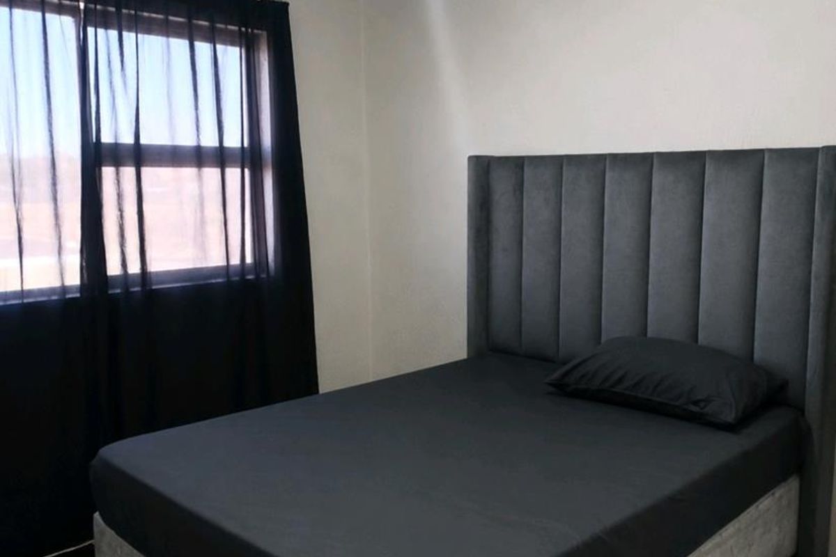 A simple bedroom featuring tiled flooring and a window with dark curtains.