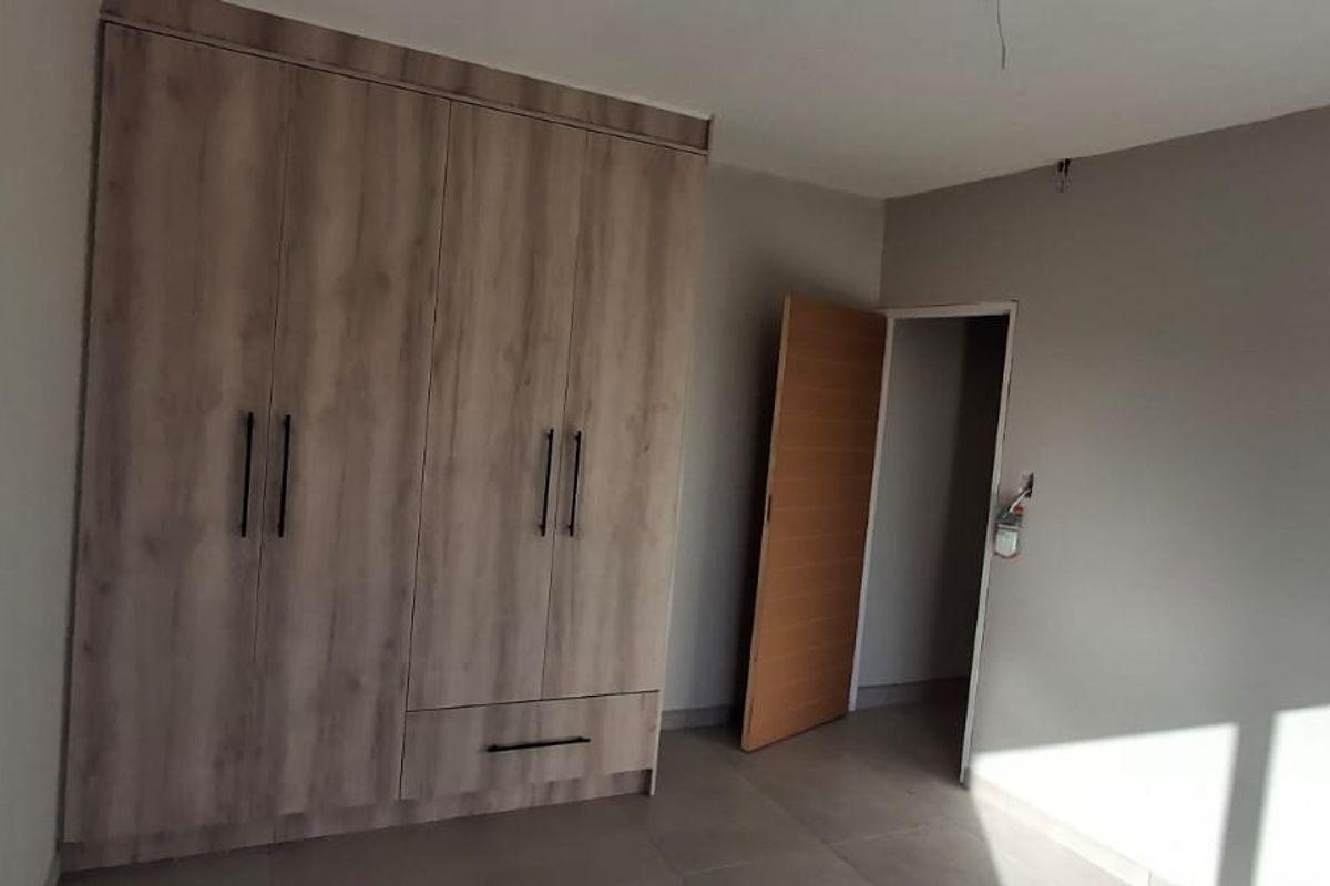 A clean, modern bedroom featuring neutral wall tones, tiled flooring, and a large built-in wardrobe with contemporary hardware.