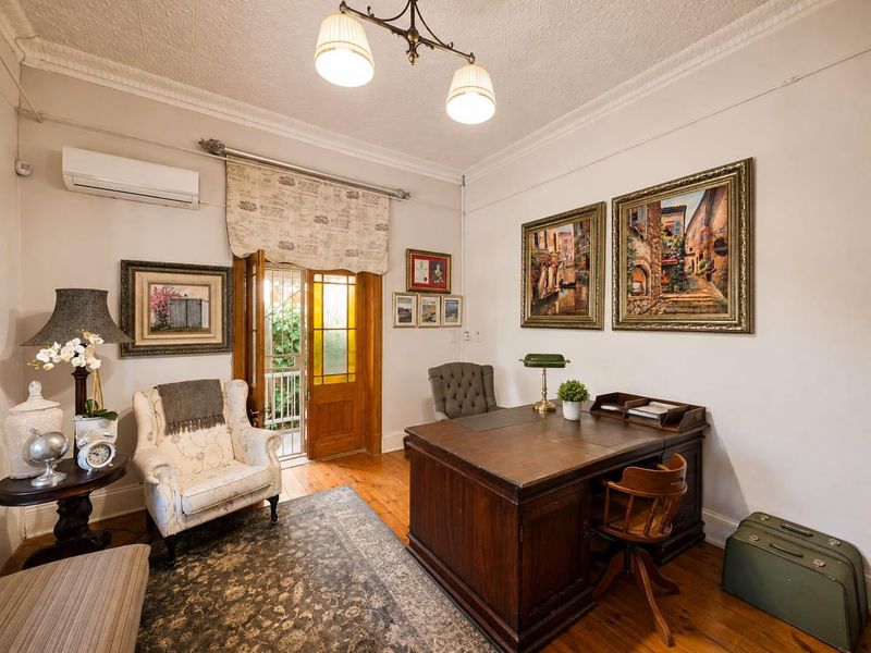 A well-maintained home office featuring polished timber flooring, decorative ceiling cornicing, and direct access to an outdoor area via a timber-framed glass door.