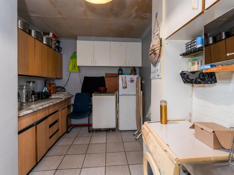 A dated kitchen featuring laminate cabinetry, tiled flooring, and built-in storage, currently showing signs of wear and requiring cosmetic updates.
