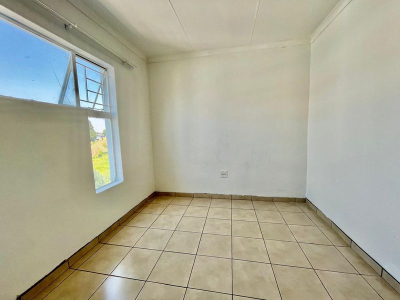 An empty bedroom featuring tiled flooring, white walls, and an aluminium window with security bars.