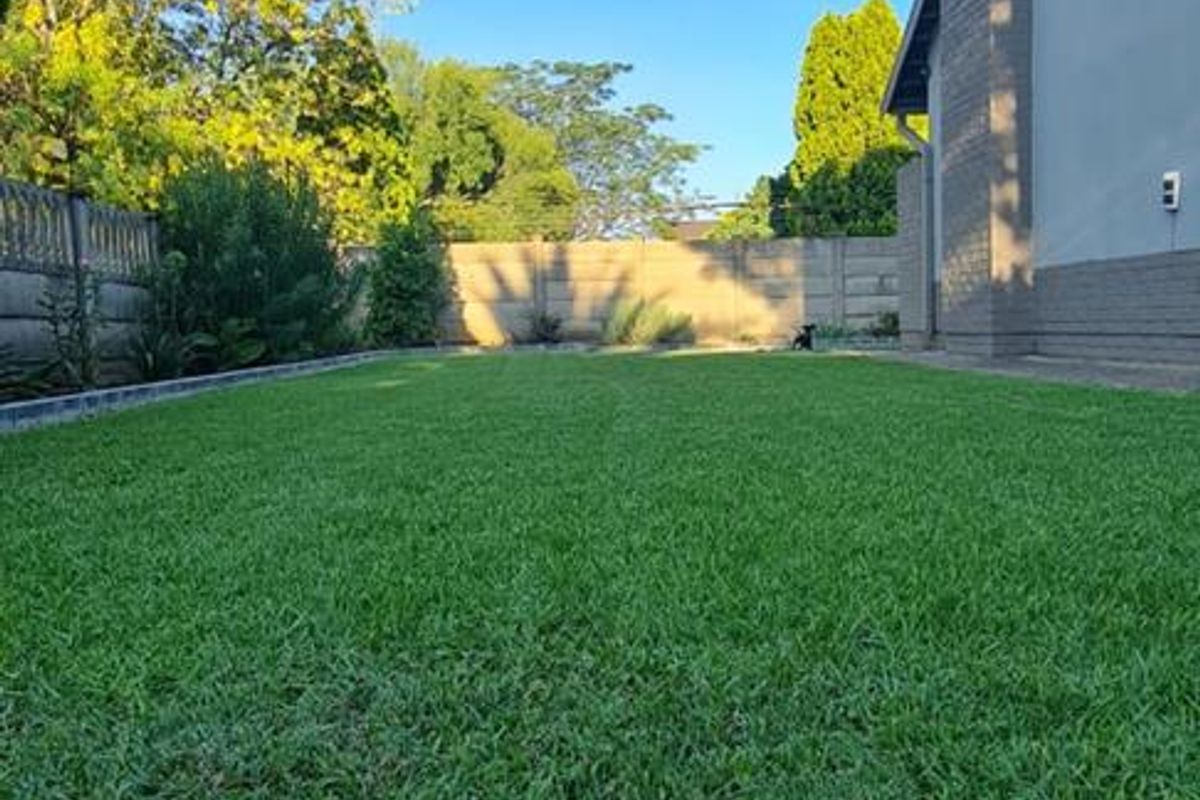 A well-maintained rear garden featuring a lush green lawn and a secure precast concrete boundary wall.