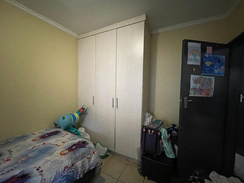 A bedroom featuring a built-in wardrobe, tiled flooring, and neutral wall finishes.