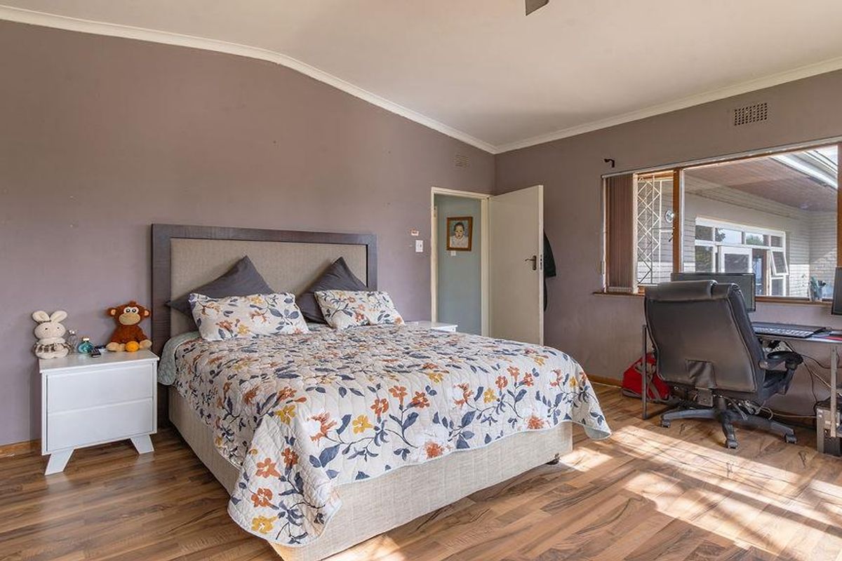 Spacious bedroom featuring laminate flooring, a ceiling fan, and large windows with security gates, offering a functional layout with neutral wall tones.