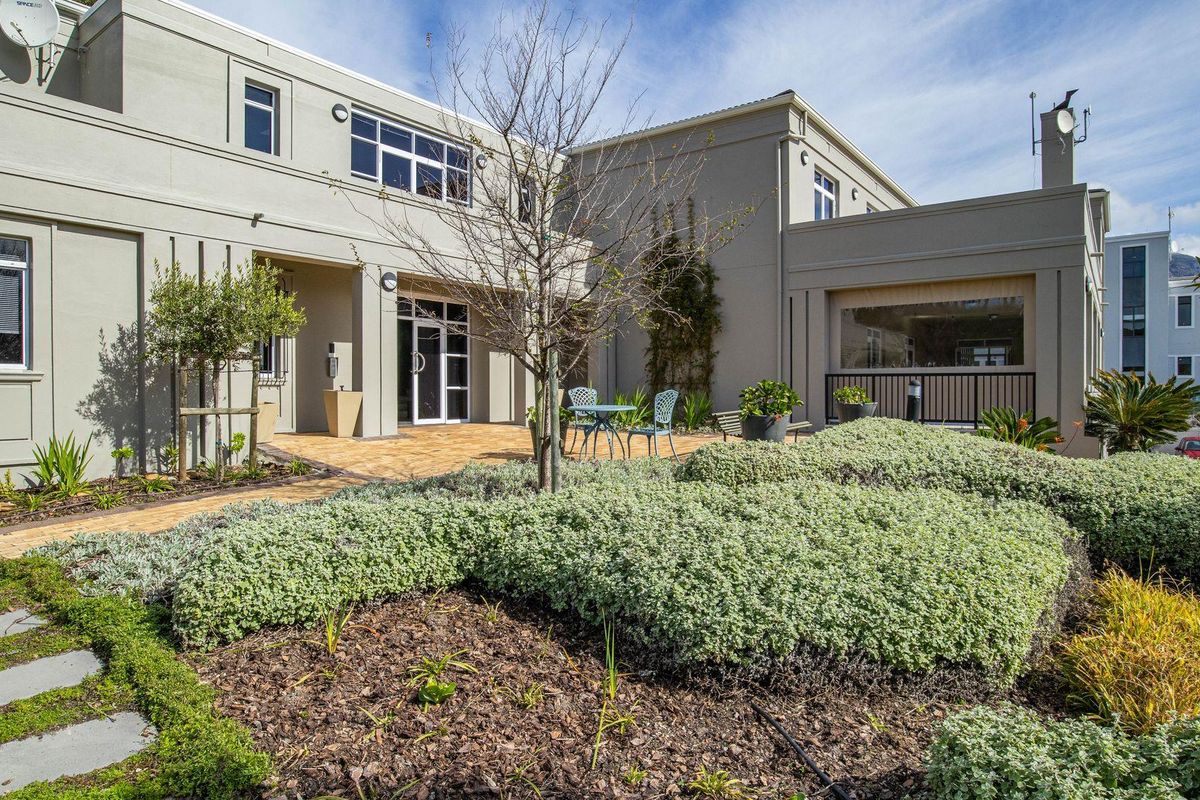 A well-maintained office building exterior featuring a paved courtyard, landscaped garden beds, and modern architectural facade with large windows.