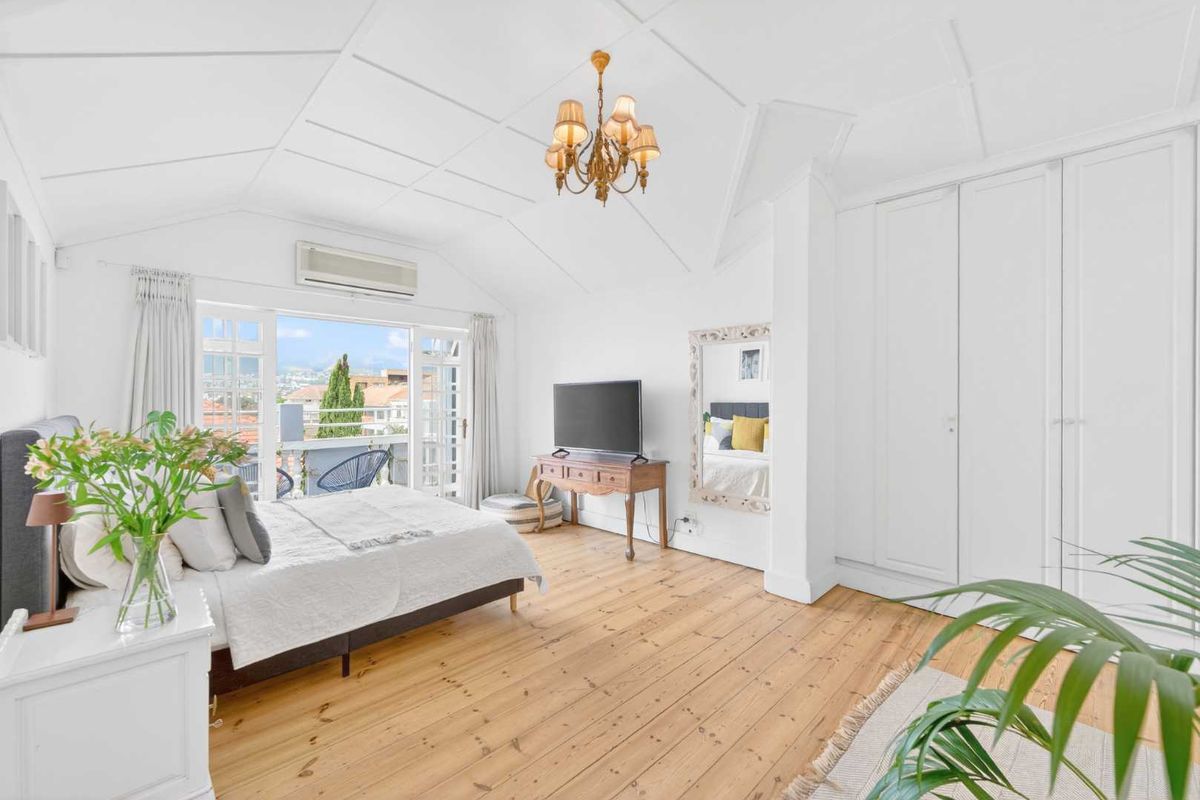 Spacious bedroom featuring vaulted ceilings, polished timber flooring, built-in wardrobes, and direct access to a private balcony with views.