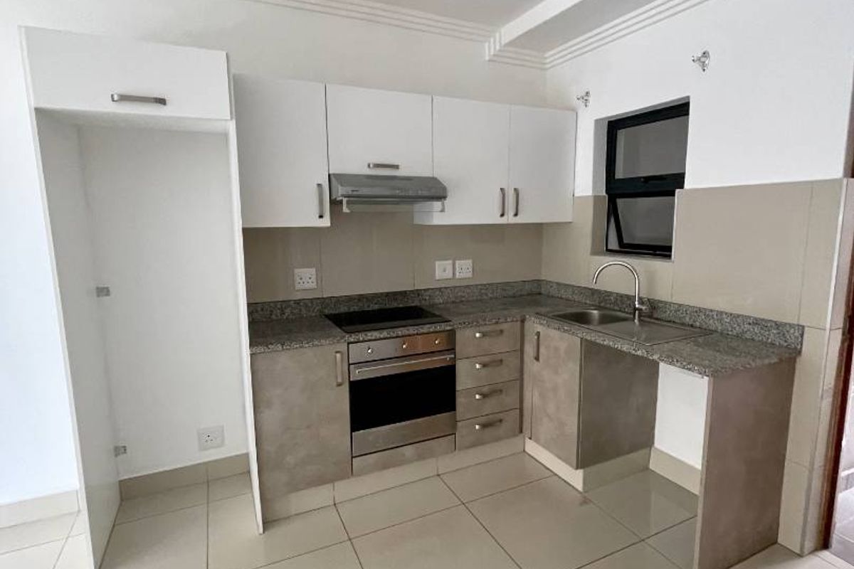 A modern kitchen featuring granite countertops, built-in oven and hob, extractor fan, and tiled flooring with ample cabinetry.