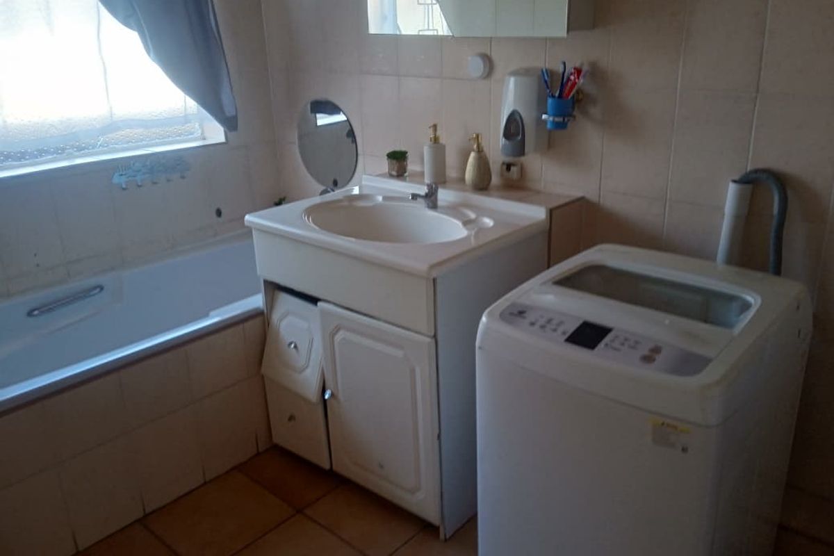 A functional bathroom featuring a built-in bathtub, vanity basin with storage cabinet, and dedicated space for a top-loading washing machine.