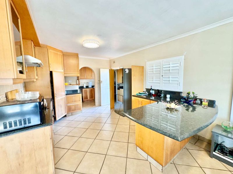 Spacious kitchen featuring wooden cabinetry, granite countertops, tiled flooring, and an integrated breakfast bar, offering a functional layout with classic design elements.