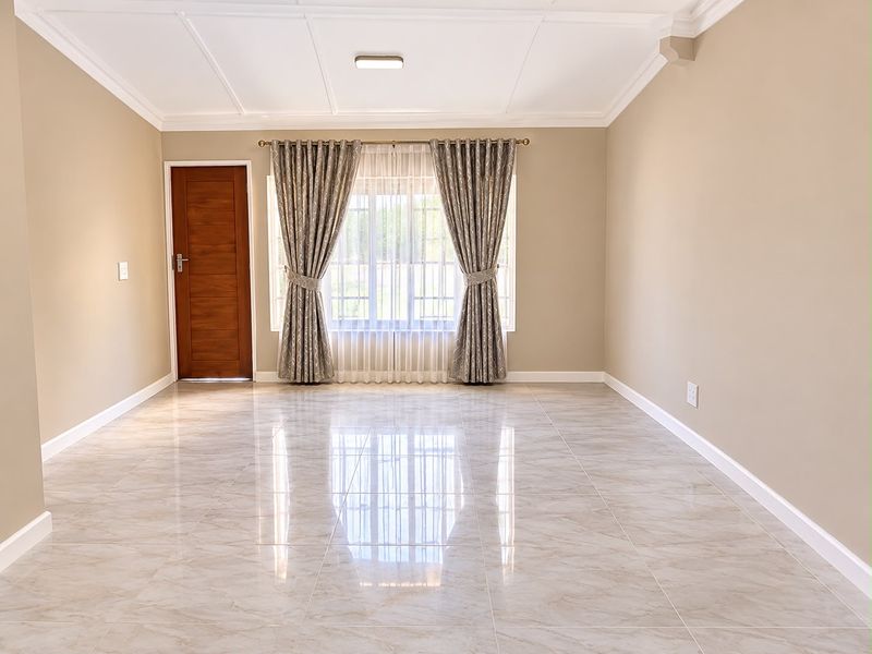 A bright, empty living room featuring polished marble-look floor tiles, a coffered ceiling, and a wooden door, offering a clean and modern blank canvas.