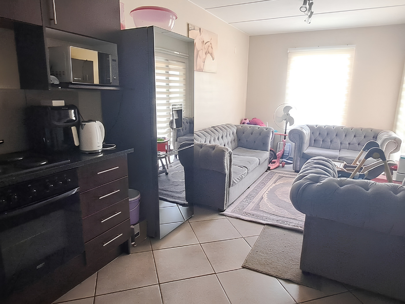 An open-plan living area featuring a compact kitchen with built-in cabinetry, electric stove, and oven, seamlessly flowing into the lounge space with tiled flooring.