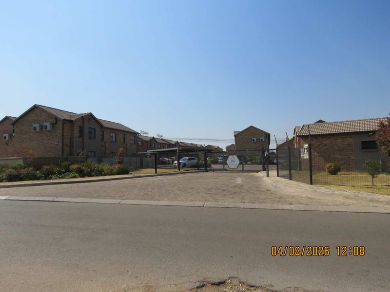View of the townhouse complex entrance featuring a paved driveway, secure gated access, and perimeter fencing.