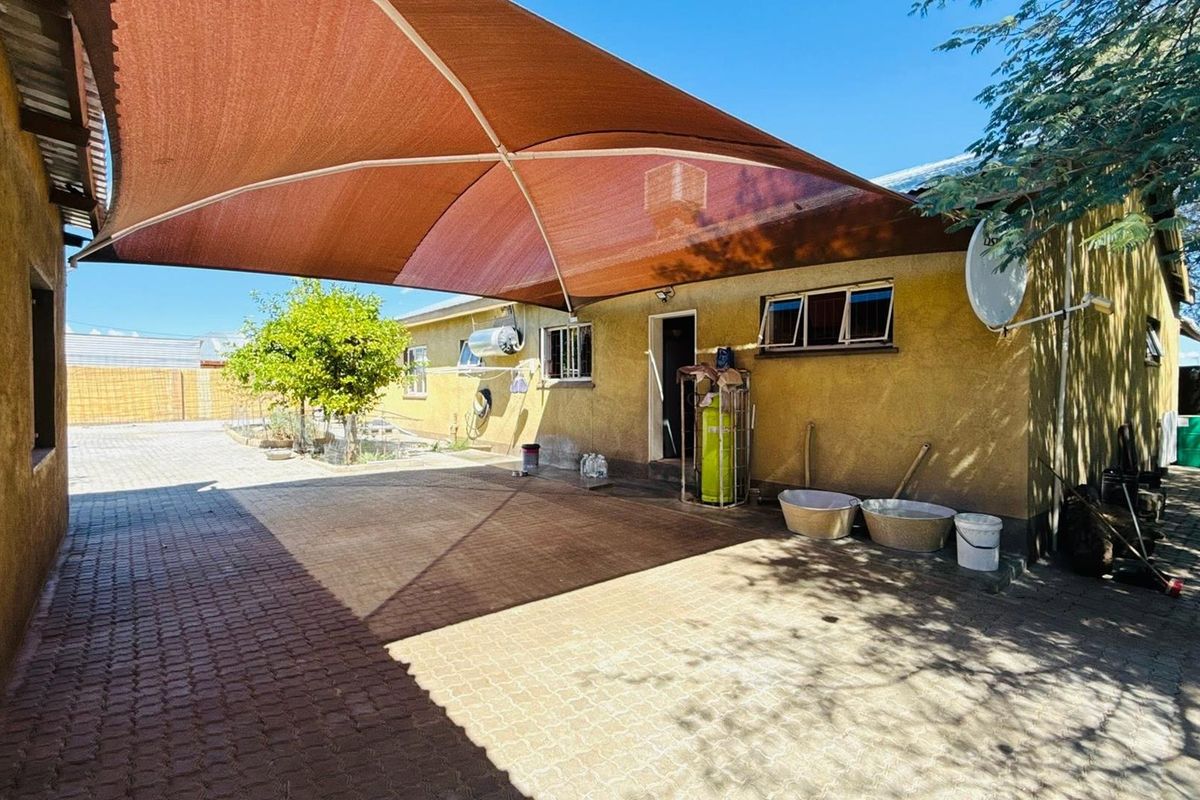 Rear exterior area featuring a paved courtyard covered by a large shade sail, providing a functional outdoor space with wall-mounted utility fixtures.