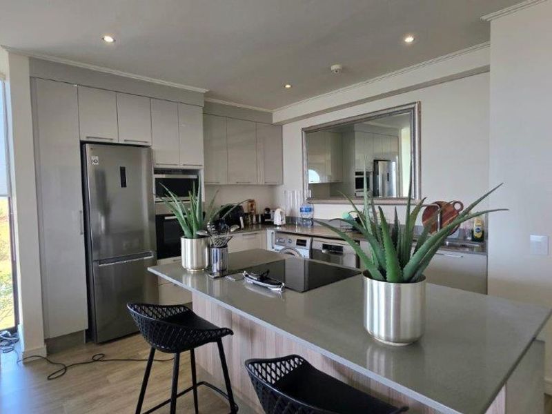 Modern kitchen featuring a central island with stone countertops, sleek gloss cabinetry, built-in appliances, and recessed lighting, offering a clean and functional workspace.