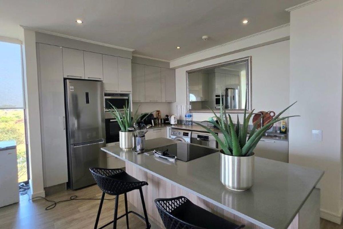 Modern kitchen featuring a central island with stone countertops, sleek gloss cabinetry, built-in appliances, and recessed lighting, offering a clean and functional workspace.