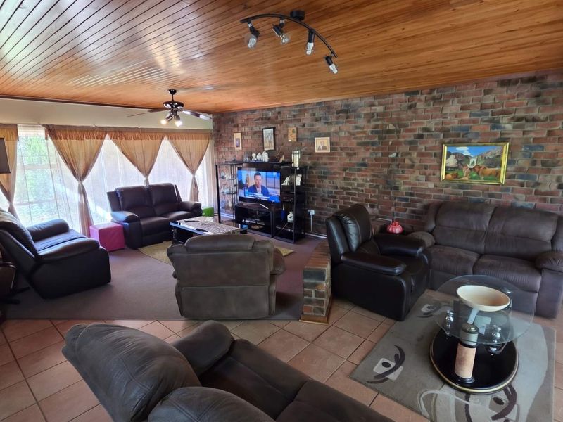 Spacious living room featuring a distinctive exposed brick wall, warm timber tongue and groove ceiling, and a combination of tiled and carpeted flooring.