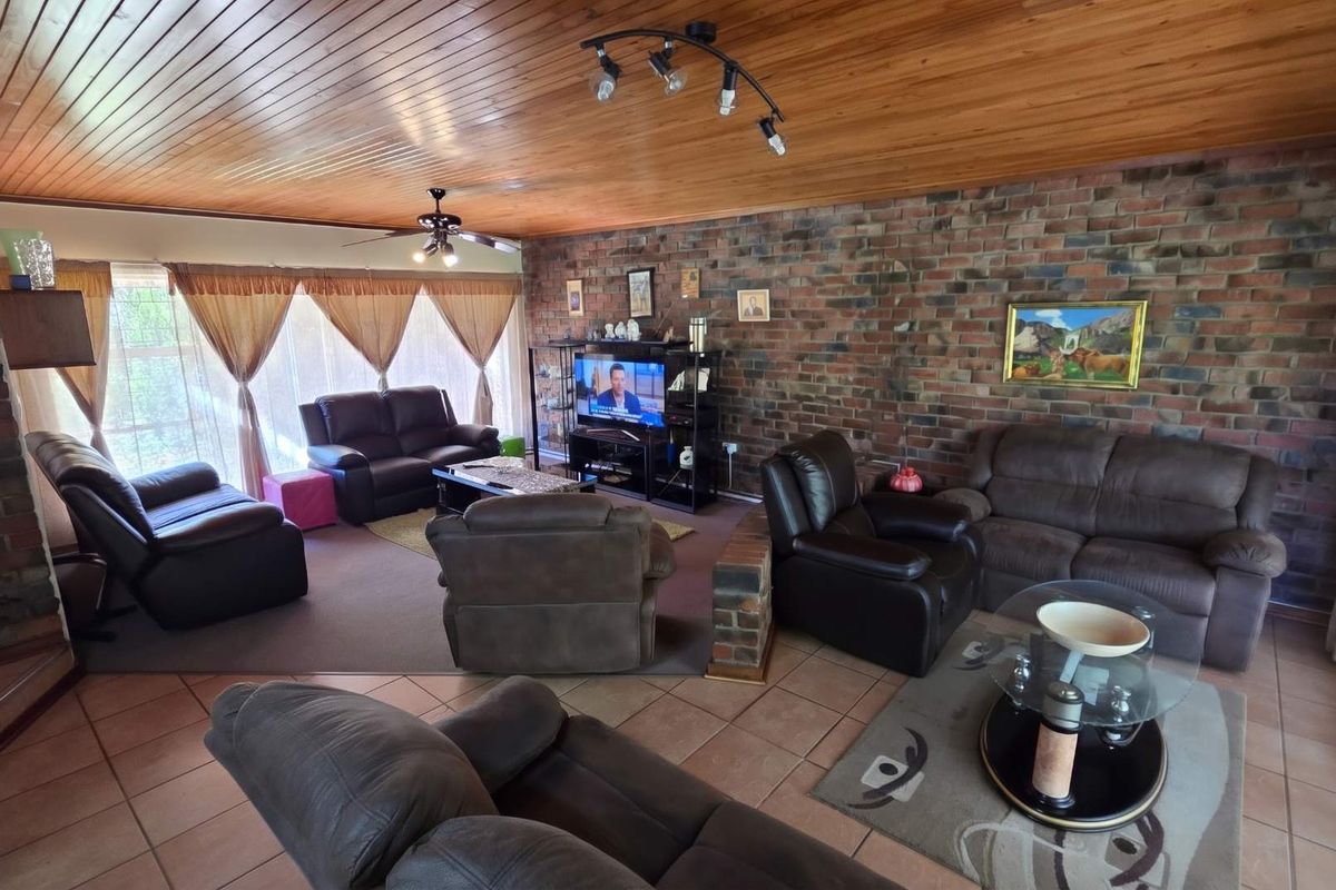 Spacious living room featuring a distinctive exposed brick wall, warm timber tongue and groove ceiling, and a combination of tiled and carpeted flooring.