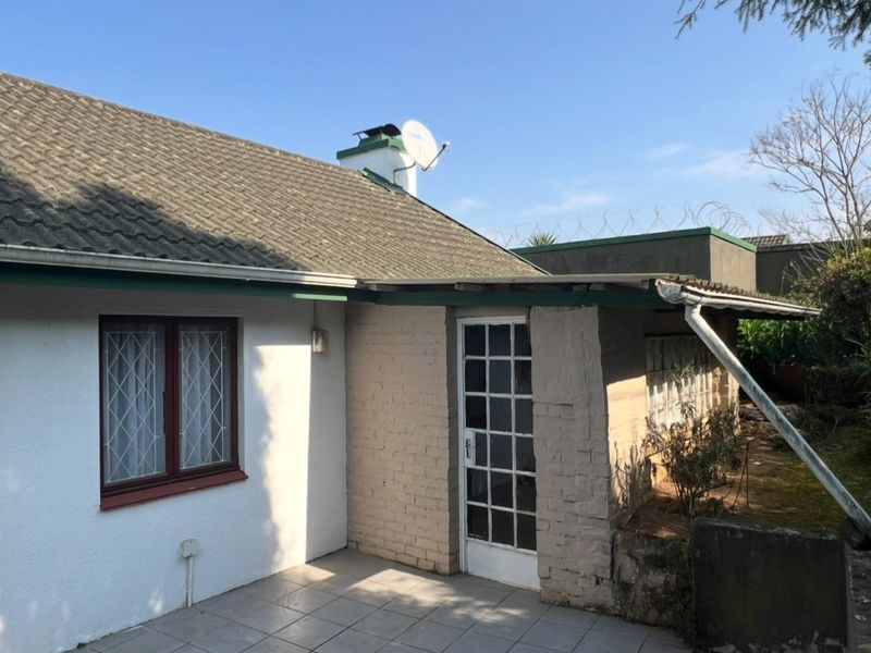 Rear exterior view of the townhouse featuring a tiled patio, brick facade, and roof with chimney and satellite dish.