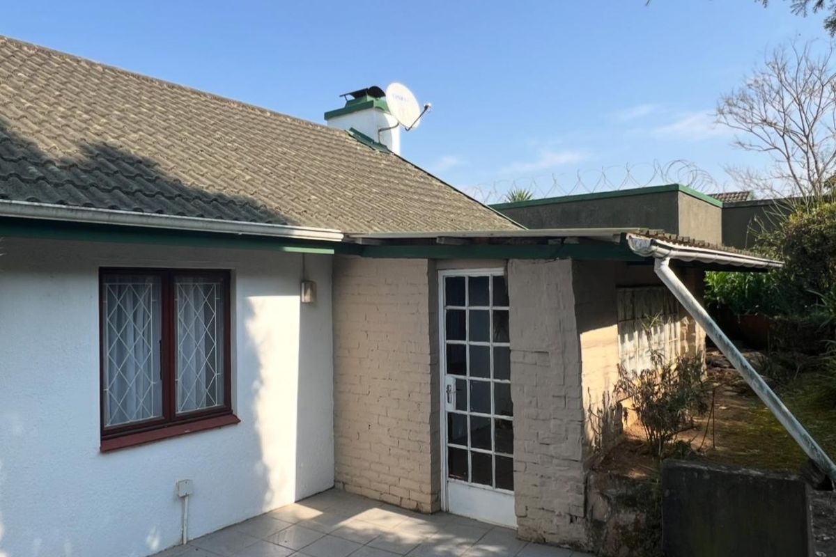 Rear exterior view of the townhouse featuring a tiled patio, brick facade, and roof with chimney and satellite dish.