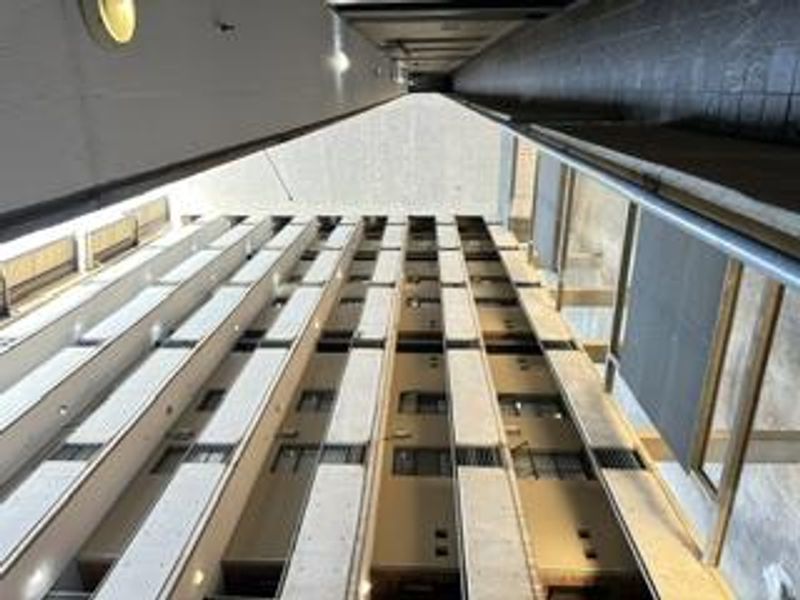 A vertical perspective view of an apartment building's central light well, featuring concrete walkways and metal railings across multiple levels.