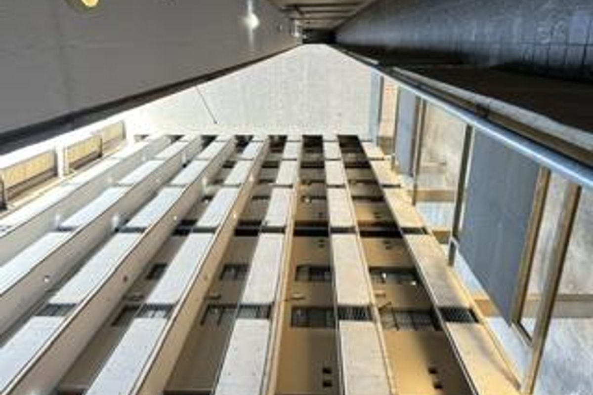 A vertical perspective view of an apartment building's central light well, featuring concrete walkways and metal railings across multiple levels.