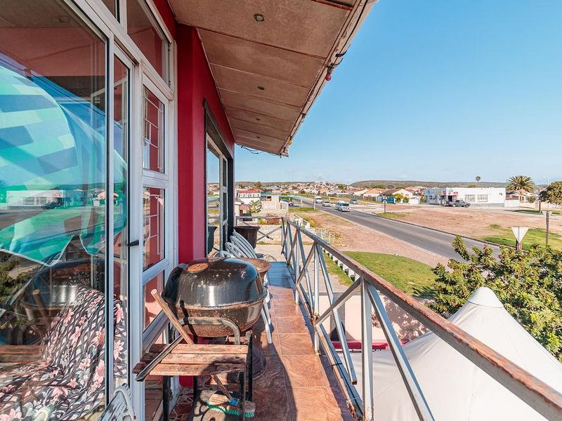 An elevated balcony featuring tiled flooring and a metal balustrade, offering an open view of the surrounding street and neighbourhood.