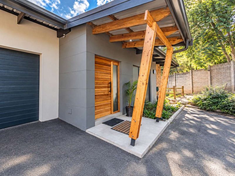Modern townhouse entrance featuring a timber front door, covered porch with timber pergola, asphalt driveway, and a sectional garage door.